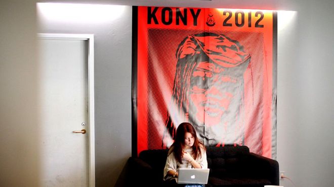 Женщина, сидящая перед плакатом Kony 2012