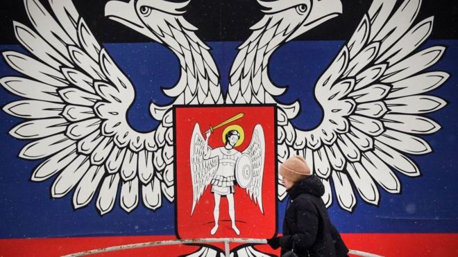 Una mujer camina frente al emblema de la República Popular de Donetsk