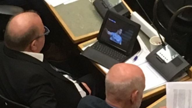 Советник лейбористской партии Кирклиса Стив Холл смотрит футбольный матч во время дебатов в муниципалитете Хаддерсфилда.