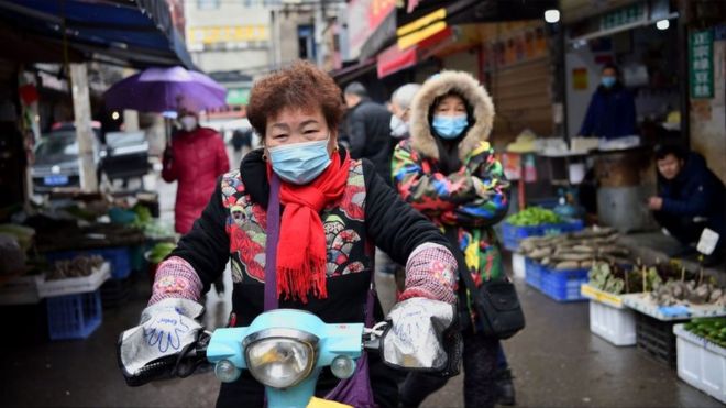 A woman wearing a face mask to help stop the spread of a deadly virus which began in the city rides her scooter through a market in Wuhan, 24 January 2020