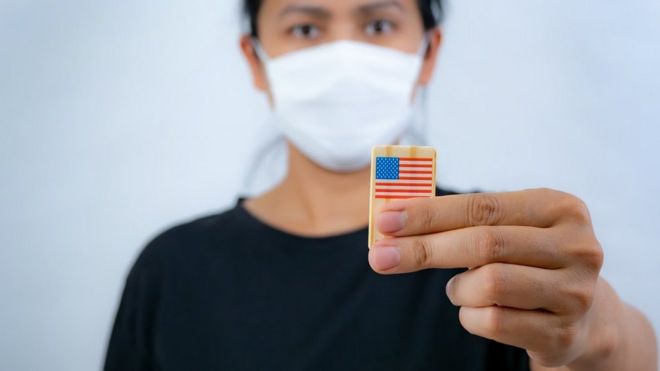 Stock photo of an Asian woman wearing a mask, holding a pin of a US flag