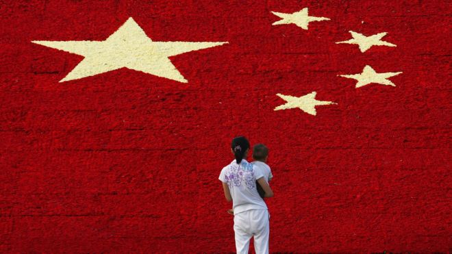 A woman holds her son as she looks at the national flag made up of 100,000 carnations at Wuling Square 25 September 2007 in Hangzhou, China.