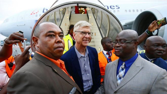Бывший футбольный тренер Арсен Венгер (С) приветствует министр молодежи и спорта Либерии Зоегар Уилсон (справа), когда он прибывает в международный аэропорт Робертс в Харбеле, Либерия, 22 августа 2018 года.
