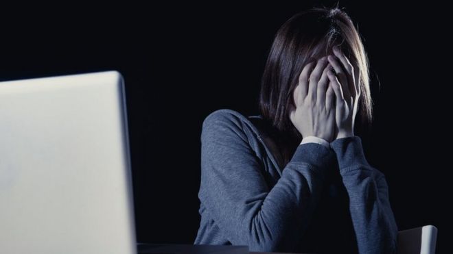 Mujer cubriéndose la cara frente a una computadora