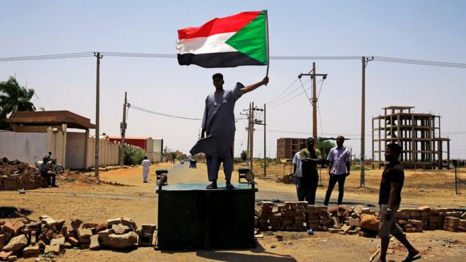 A Sudanese protester holds a national flag as he stands on a barricade along a street, demanding that the country"s Transitional Military Council hand over power to civilians, in Khartoum, Sudan June 5, 2019.