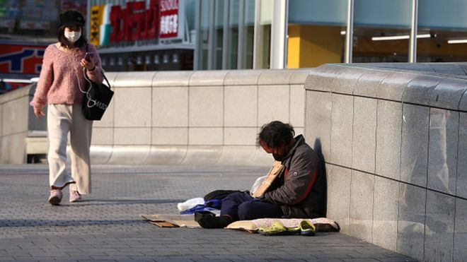 Женщина в маске проходит мимо бездомного в Осаке, Япония