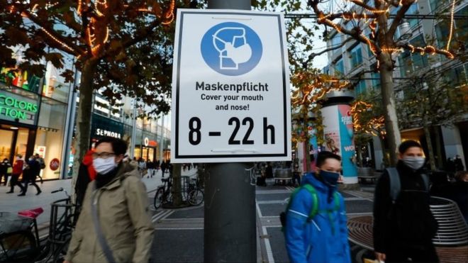 People walk past a sign reminding them to wear a face mask