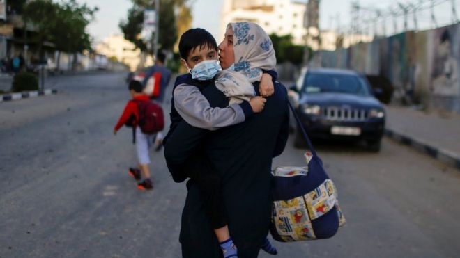 A Palestinian woman carries her son after their apartment building was hit in an Israeli air strike in Gaza City (12 May 2021)