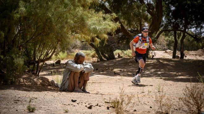Mkiambiaji aliyeshiriki mbio za kilomita 250 za Marathon de Sables akipita karibu na Kourci Dial Zaid na aliyeketi chini ya kivuli ni Jebel El Mraïer eneop la kusini mwa jangwa la sahara nchini Morocco, Jumanne tarehe 9 Aprili 2019