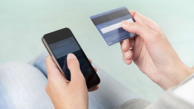 Pessoa segura o cartao de credito em uma mao e o celular na outra