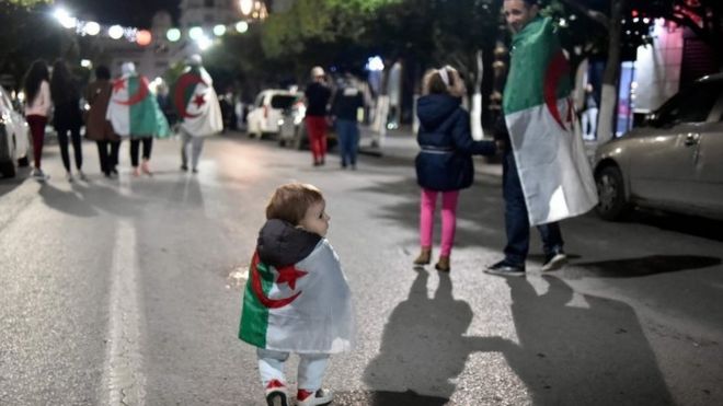 В Алжире празднует маленький ребенок, накинутый на национальный флаг Алжира. Фото: 2 апреля 2019 года
