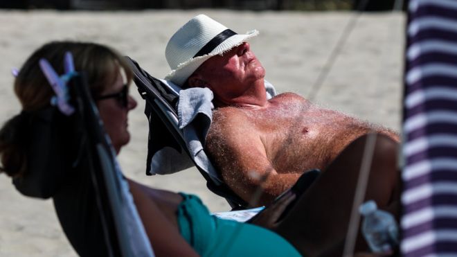 Мужчина лежит на солнышке на британском пляже, а на животе выставлен живот