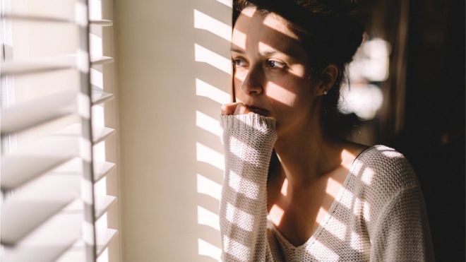 Mujer temerosa frente a la ventana