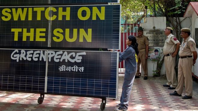 Индийские полицейские смотрят, как активист Гринпис блокирует вход в резиденцию министра энергетики Дели Харуна Юсуфа с батареей солнечных батарей в Нью-Дели