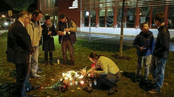 Люди зажигают свечи и кладут цветы после того, как человек в маске, владеющий чем-то, похожим на меч, ранил четырех человек в школе в Трольхеттане, Южная Швеция, 22 октября 2015 года.