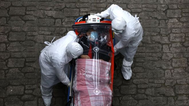 Paciente de coronavirus transportado en camilla por personal de salud.
