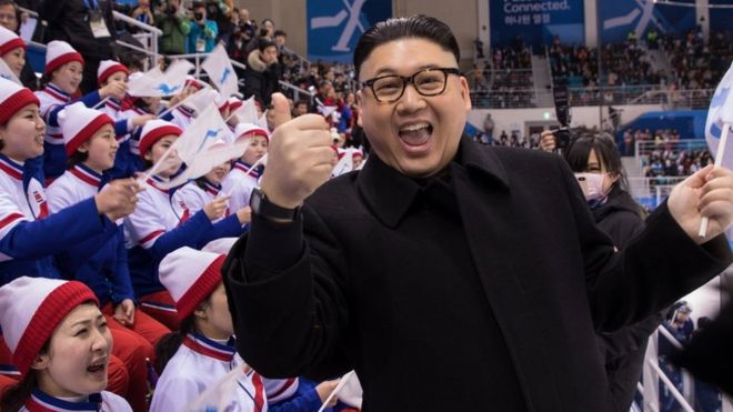 A Kim Jong-un impersonator gives a thumbs-up to the camera as Korea fans look on angrily
