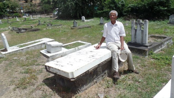 Джо Суини сидит на могиле, где похоронен его предок на кладбище Карр-Бэй в Монтсеррате