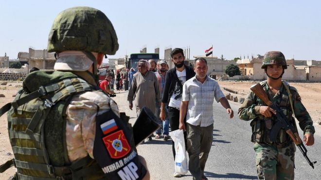 Русский солдат стоит на страже, когда люди проходят на контролируемую правительством территорию на контрольно-пропускном пункте Абу-Духур на восточной окраине провинции Идлиб, Сирия (25 сентября 2018 года)