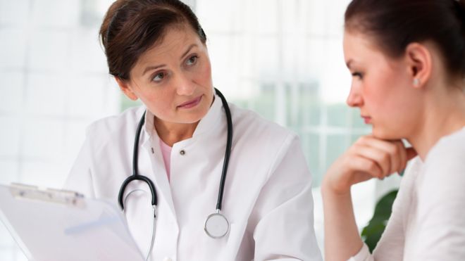Una mujer joven escuchando a una doctora durante una consulta médica