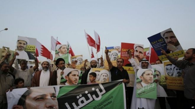 Мужчины и мальчики выкрикивают лозунги и поднимают национальные флаги и плакаты шейха Али Салмана во время акции протеста в Бахрейне 16 июня 2015 года