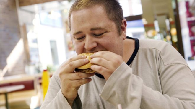 Человек ест гамбургер быстрого питания