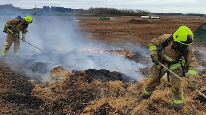 Two firefighters prodding burning hay with a long stick