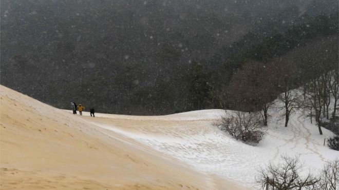 Люди идут по частично покрытой снегом песчаной дюне Пила после снегопада 28 февраля 2018 года в Ла-Тест-де-Бюш, на юго-западе Франции