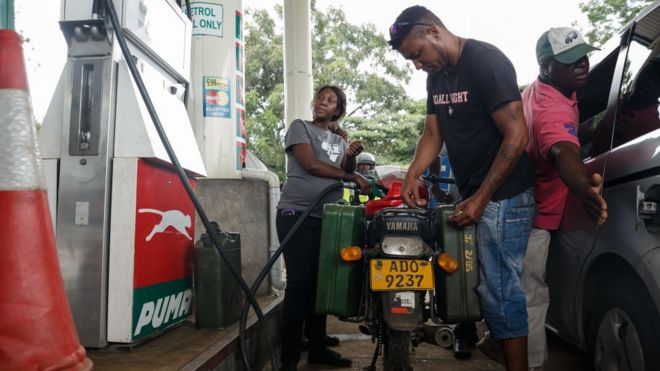 A petrol attendant serves a motorcyclist with two jerry cans attached to his motorbike at a fuel station,