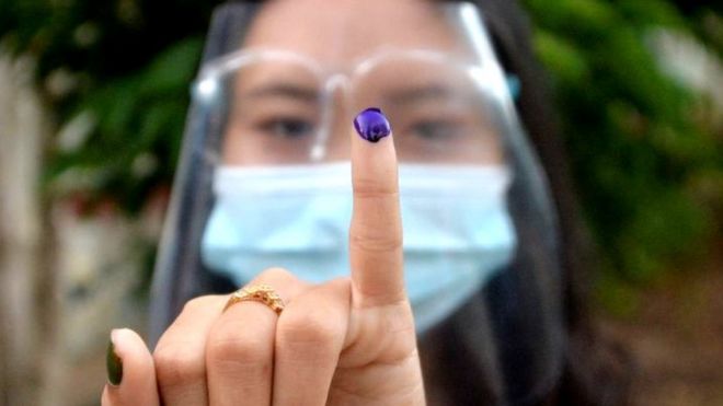 Woman holds up little finger covered in indelible ink after voting