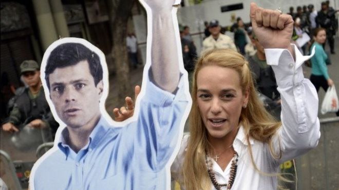 Жена арестованного лидера оппозиции Леопольдо Лопеса, Лилиан Тинтори, поднимает кулак рядом с плакатом мужа перед зданием венесуэльского суда в Каракасе 23 июля 2014 года.