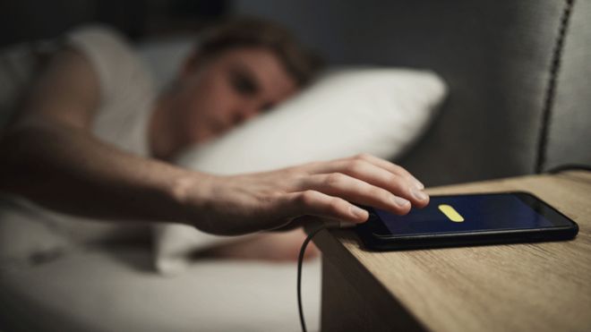 A person putting mobile beside the bed