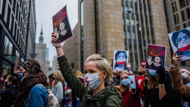 A woman wears a protective face mask and holds a banner as she participates in a National strike for the seventh day of protests against the Constitutional Court ruling