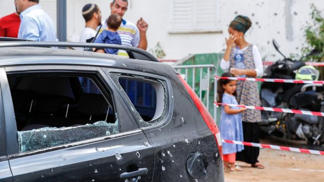 Израильтяне стоят возле автомобиля, поврежденного ракетой, выпущенной из Газы (9 августа 2018 года)