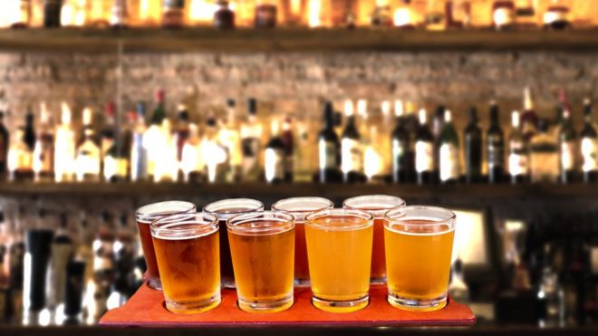 Пивной полёт из восьми пробных бокалов крафтового пива на барной столешнице.