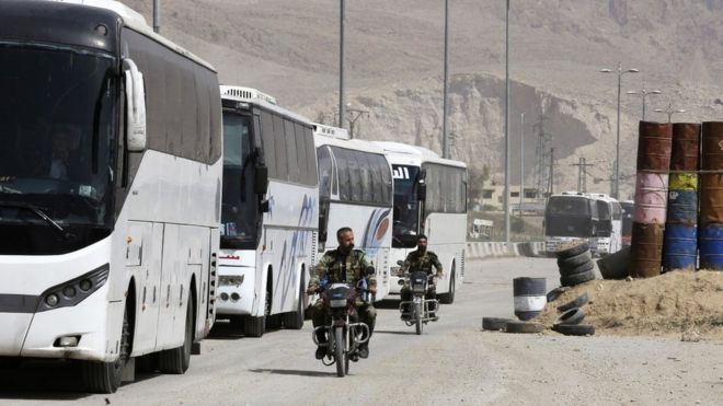 Syrian government forces drive motorbikes past buses waiting at the entrance of Harasta in the rebel-held Eastern Ghouta (22 March 2018)