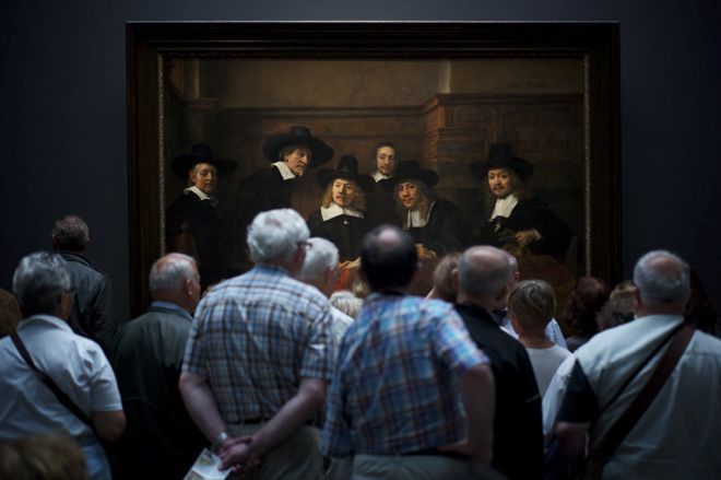 Museum visitors watching Rembrandt's painting Syndics of the Drapers' Guild