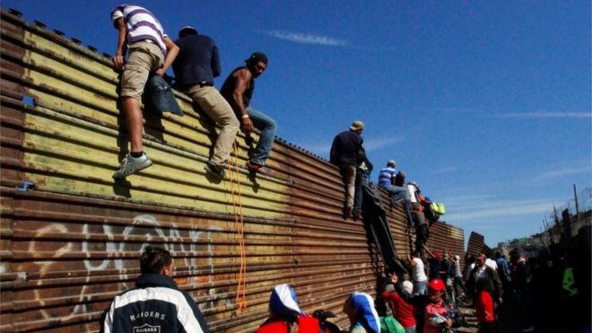 Мигранты поднимаются на пограничный забор между Мексикой и Соединенными Штатами