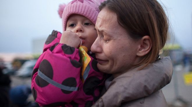 Mujer refugiada llora con su niña pequeña en brazos