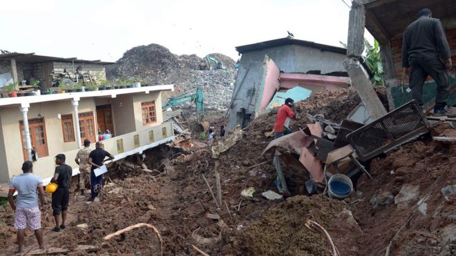 Жители Шри-Ланки проходят через разрушенные дома на месте обрушившейся мусорной свалки в Коломбо 15 апреля 2017 года.
