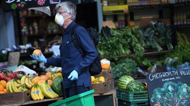 Мужчина в маске покупает апельсины на рынке Боро в Лондоне, Великобритания, 5 июня 2020 года. С 1 июня британское правительство заявило, что некоторым предприятиям, включая рынки под открытым небом, разрешена торговля.