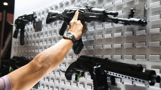 Um participante do encontro anual da NRA em 2022 no Texas analisa rifles semiautomáticos em exposição