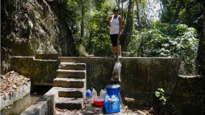 Женщина смотрит на бутылки и ведра, наполненные водой с горы, во время отключений, которые воздействуют на водяные насосы 12 марта 2019 года в Каракасе, Венесуэла
