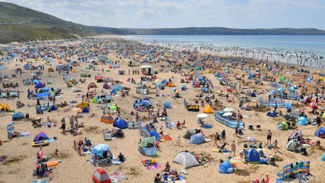 Люди на Woolacombe Beach в Северном Девоне, как еще одно заклинание теплой погоды, поражают Великобританию