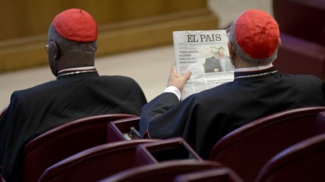 Кардинал, посещающий Синод семьи, читает газету с изображением епископа-гея Кшиштофа Чарамса и его напарника Эдуарда перед началом утреннего заседания (09 октября 2015 года)