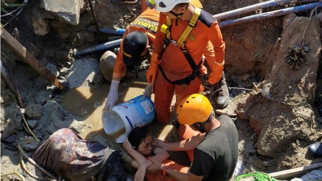 Поисково-спасательные работники помогают спасти человека, попавшего в обломки после землетрясения и цунами в Палу