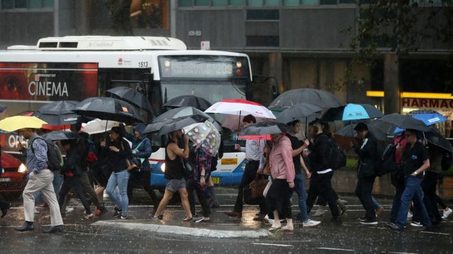 Crowd of commuters hold umbrellas as they walk through heavy rain in central Sydney