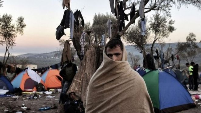 A man with a blanket wrapped around his head and shoulders stands near tents where refugees and migrants live in a field outside the Moria registration center on the Greek island of Lesbos on November 11, 2015