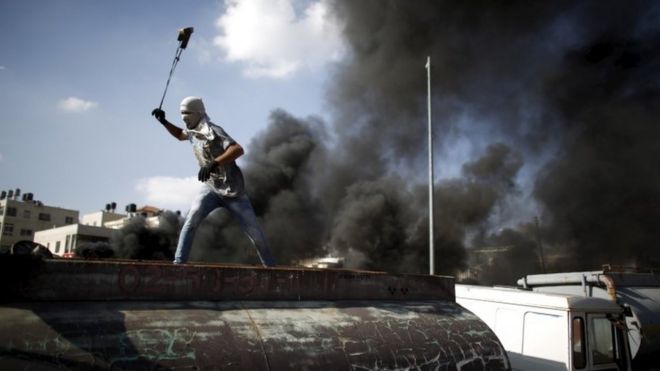 Палестинский протестующий швыряет камни в израильские войска во время столкновений возле еврейского поселения Бейт-Эль возле Рамаллаха, 15 октября 2015 года