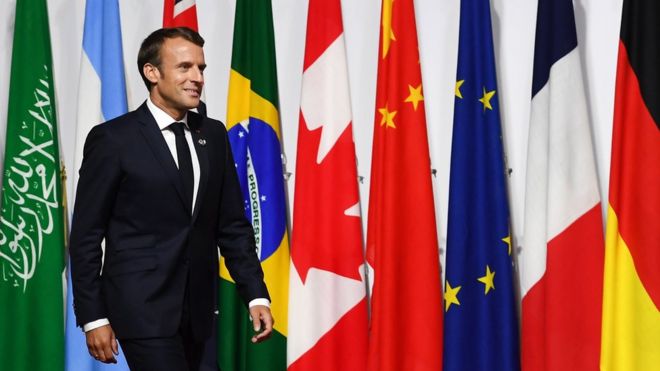 O presidente francês Emmanuel Macron passa pelas bandeiras dos países participantes do encontro do G20 em Osaka, no Japão